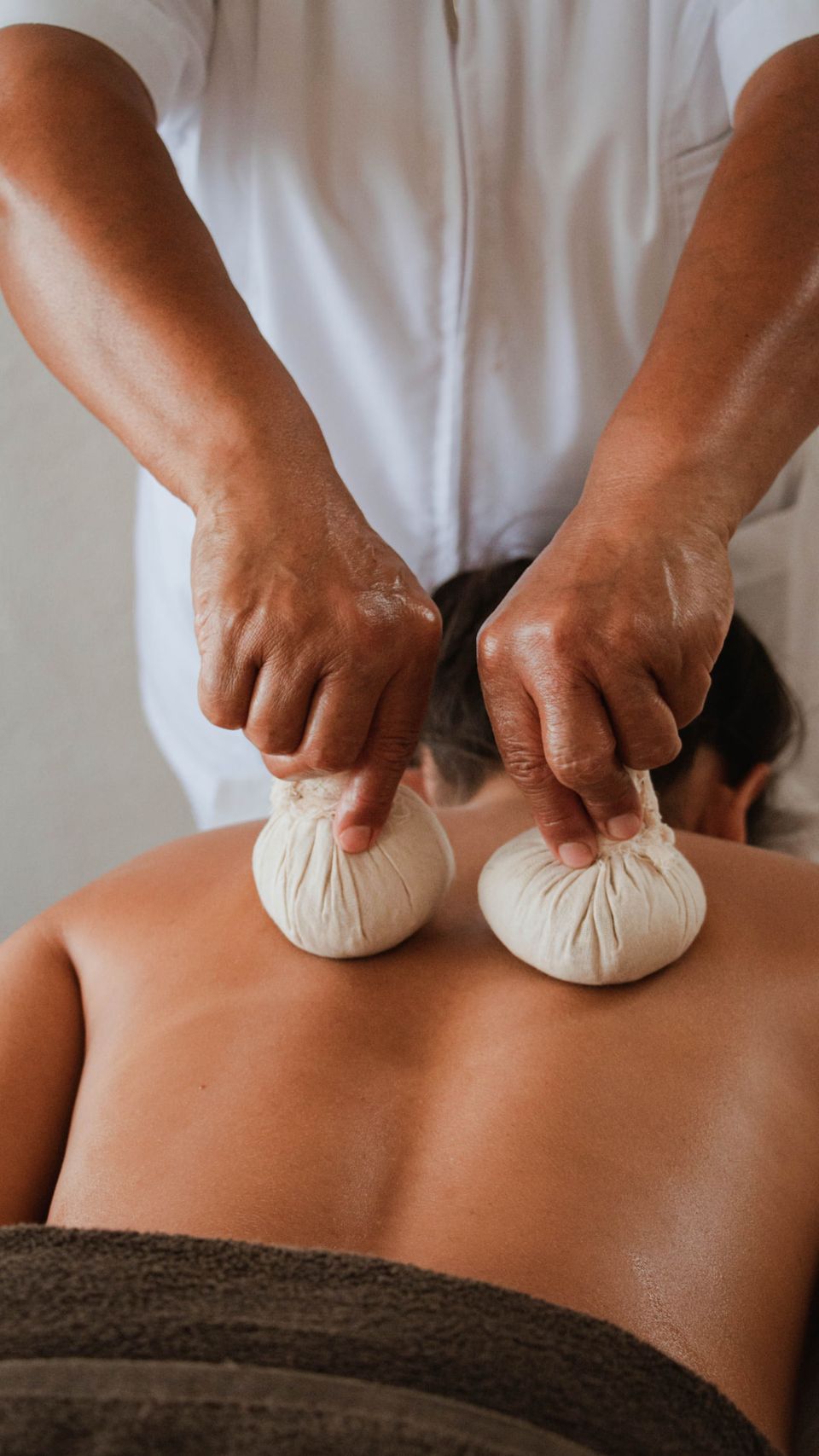 A therapist pressing warm herbal kizhi pouches along a client's back