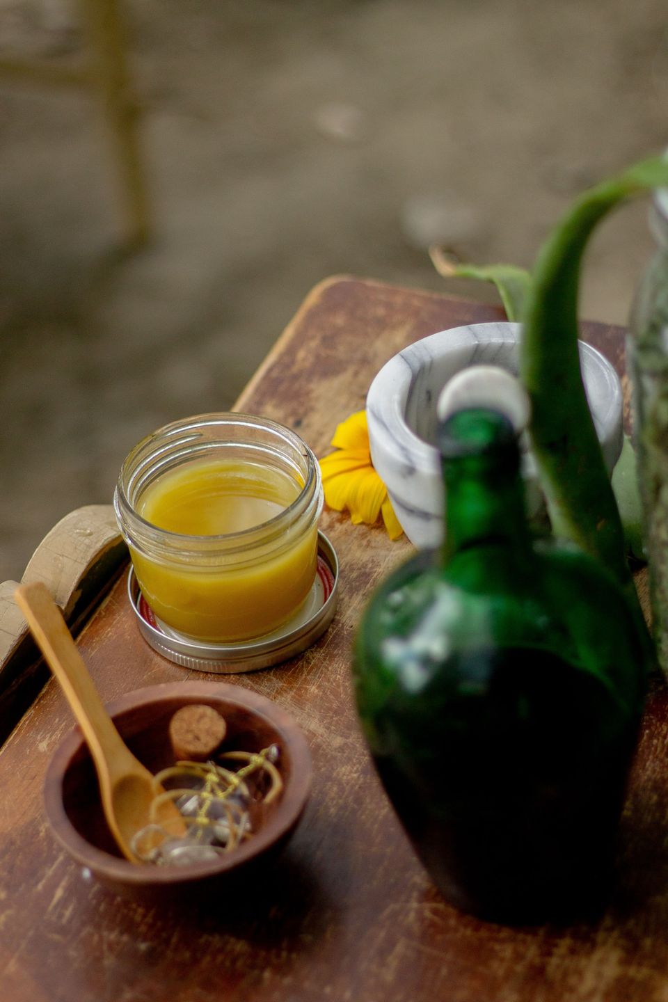 A jar of herbal balm, mortar and pestle and herbs on a wooden tray